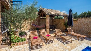 A stone patio with wooden loungers, a hammock, and a pool. - Apartment Andre Poreč - Two Bedroom Apartment with Terrace and Pool (Nova Vas)