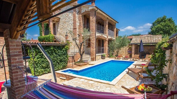 A pool area with a hammock, a stone patio, and a house with a stone facade. - Apartment Andre Poreč - Two Bedroom Apartment with Terrace and Pool (Nova Vas)