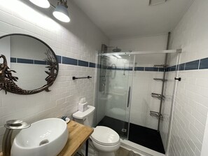 A bathroom with white tiled walls, a wooden vanity, a round mirror, a toilet, and a glass-enclosed shower. - 🛥️🛥️Boat House in Weeki Wachee-10 minute easy paddle to main river (Spring Hill)