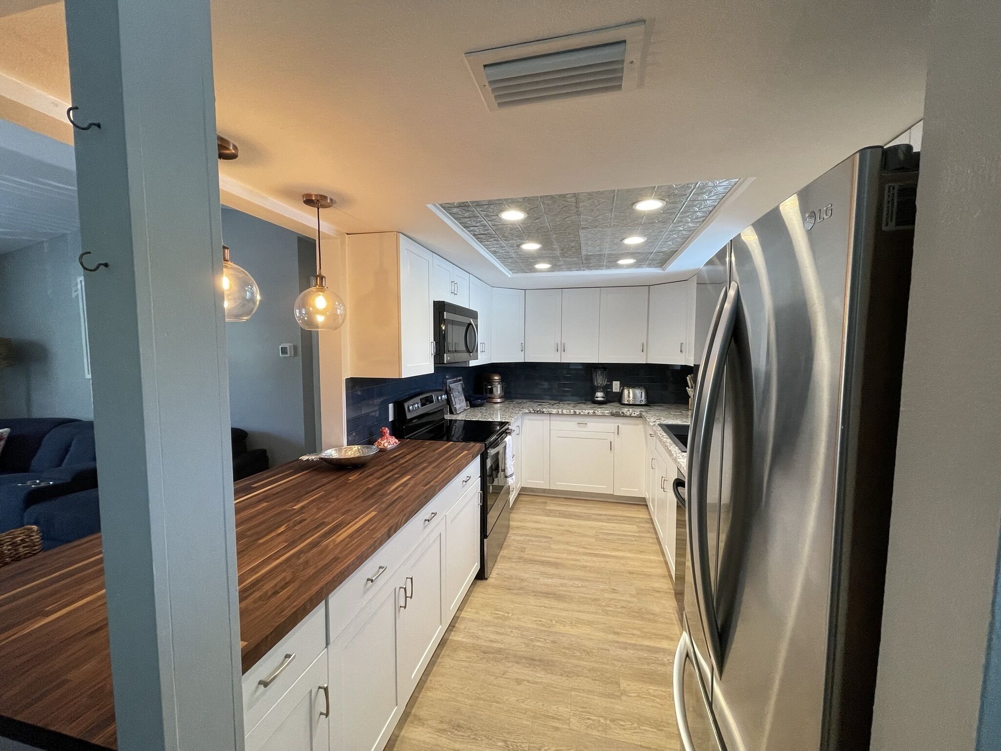 A modern kitchen with white cabinets, a wooden countertop, stainless steel appliances, and pendant lighting.