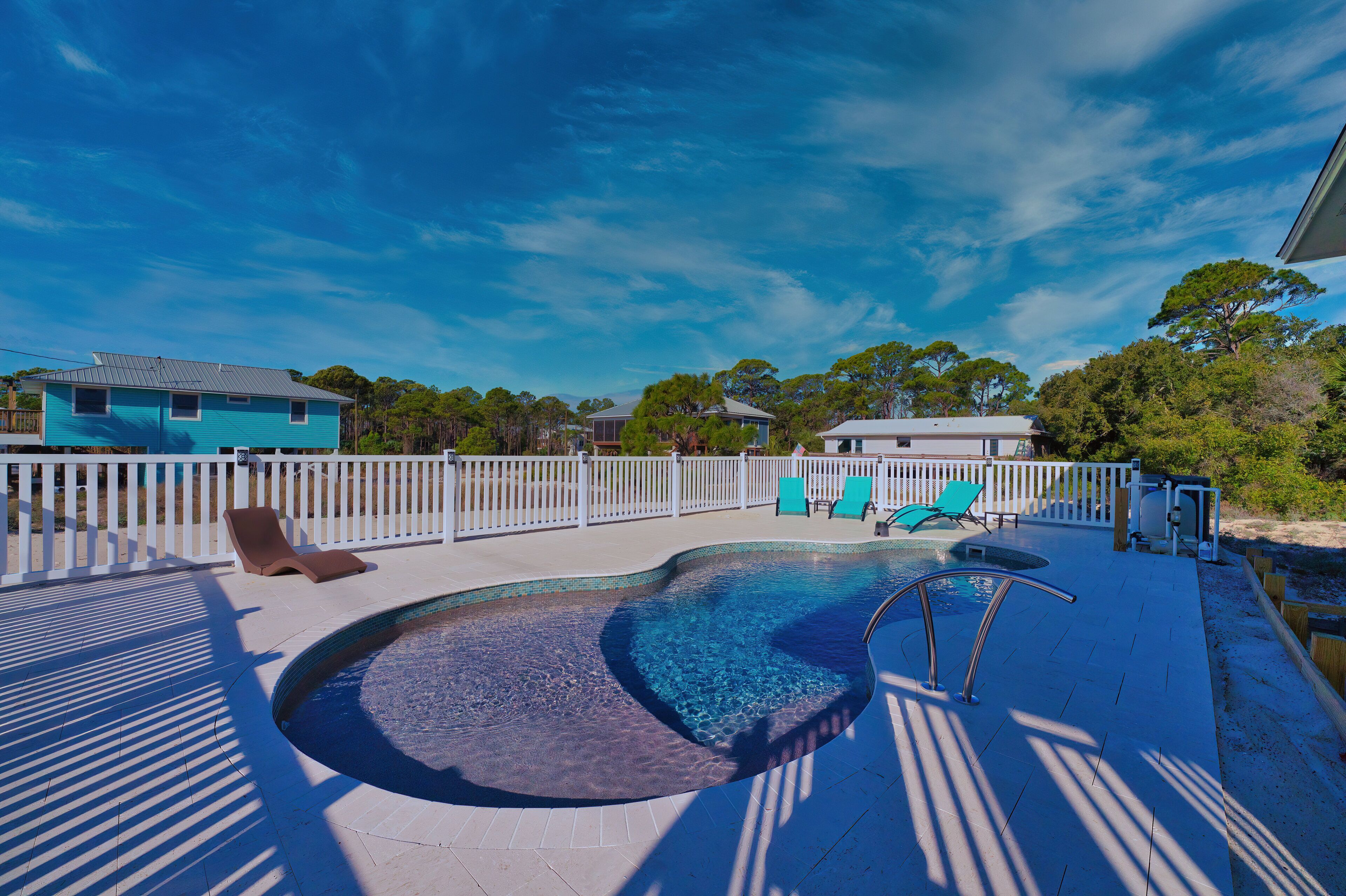 A swimming pool with lounge chairs and a white fence.