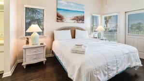 Une chambre à coucher avec un grand lit, deux tables de chevet avec des lampes, un tableau au-dessus du lit et une vue par la fenêtre.