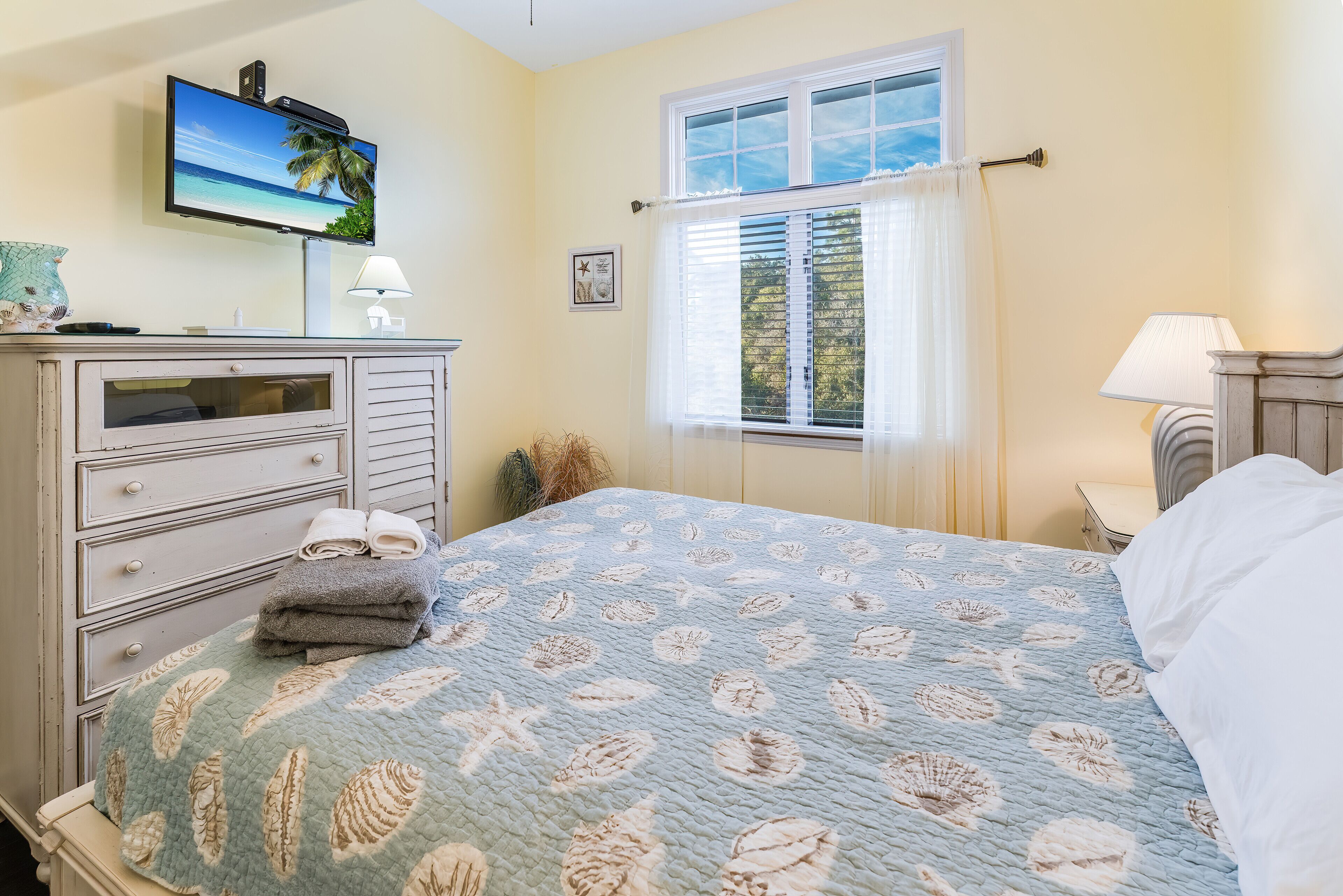 A bedroom with a bed, a dresser, a television, and a window with curtains.