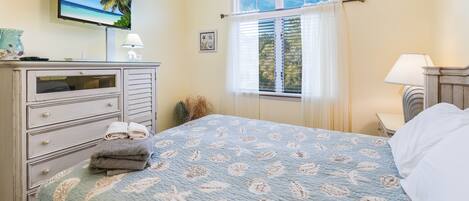 A bedroom with a bed, a dresser, a television, and a window with curtains.