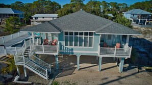 Une maison située sur la côte, dotée d’un balcon, d’une terrasse couverte et offrant une vue sur les arbres et la plage environnants.