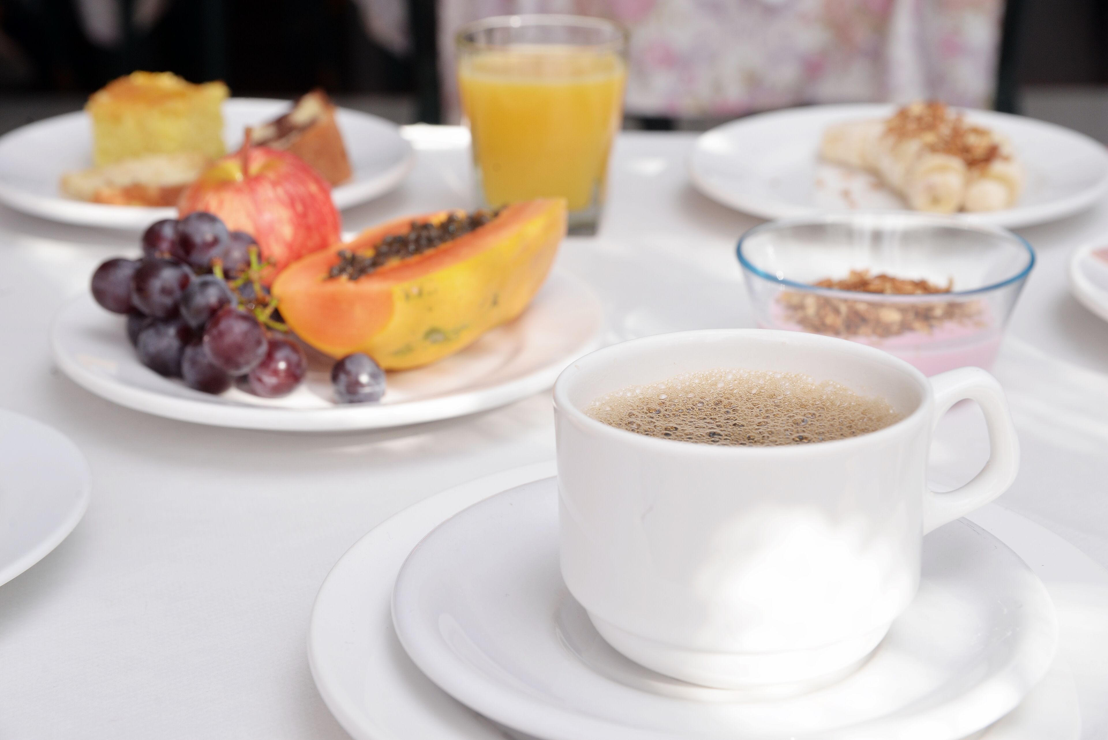 A breakfast setting with plates of fruits, a glass of orange juice, and a cup of coffee on a white table.