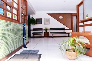 Un área de recepción con suelo de baldosas, bancos de madera, una planta en maceta y un mostrador de recepción.