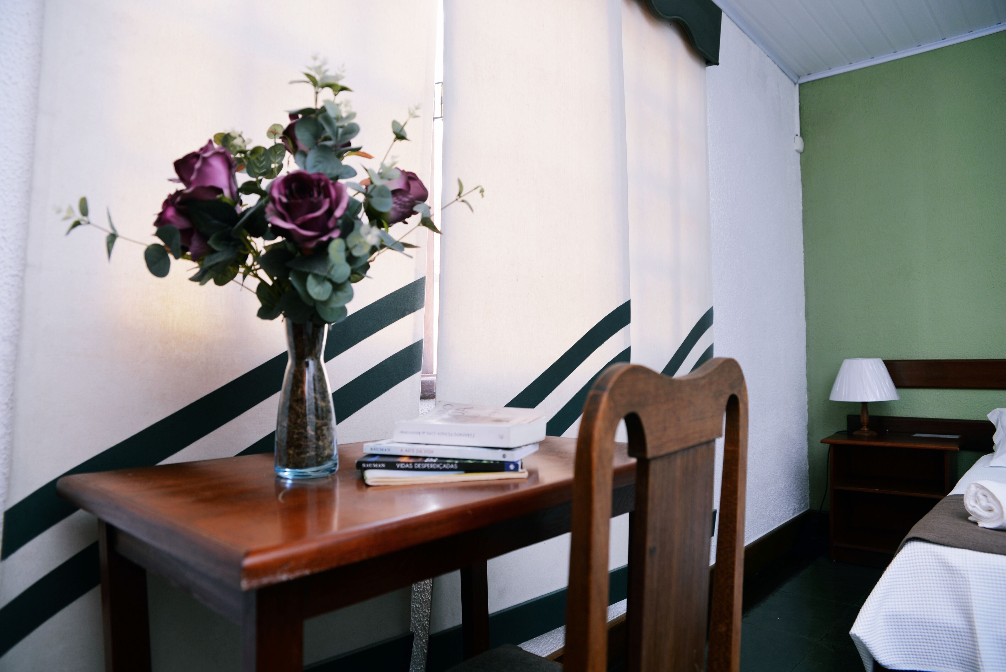 A wooden desk with a vase of flowers, a stack of books, and a chair.