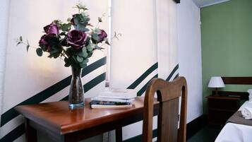 A wooden desk with a vase of flowers, a stack of books, and a chair.