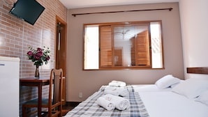 Una habitación de hotel con cama, escritorio con silla, televisor montado en la pared y ventana con persianas.
