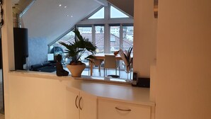 Une cuisine moderne avec une grande fenêtre, une plante en pot et un coin repas visible à travers la fenêtre.