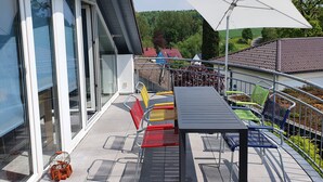 Un balcon avec une table et des chaises, un grand parasol et une vue sur les environs.