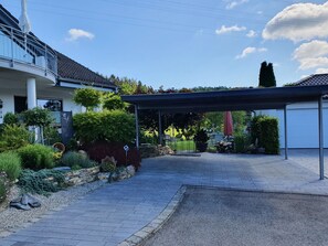 A modern house with a covered patio, a stone pathway, and various plants.
