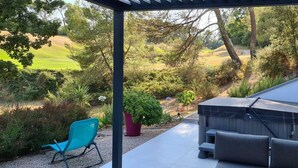 A covered patio with outdoor seating, a hot tub, and a view of a landscaped garden. - Apartment in the heart of Provence on a magnificent golf course (Flassans sur issole)