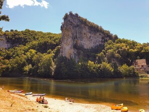A riverside view with canoes, a cliff, and a building. - 1-star furnished house 800 m from the river, near Sarlat. (Veyrignac)