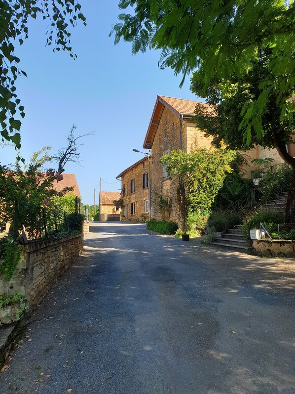 A quiet street with stone buildings, a paved road, and lush greenery.