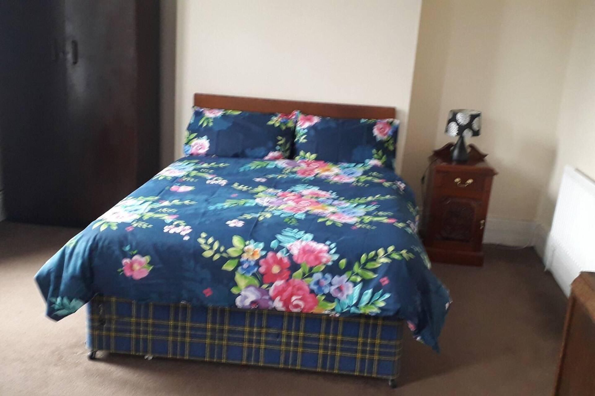 A bed with a floral duvet and a plaid skirted base.