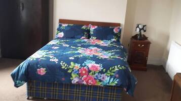 A bed with a floral duvet and a plaid skirted base.