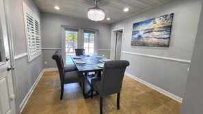 Una sala da pranzo con un tavolo imbandito per quattro persone, sedie, un lampadario e un quadro raffigurante una spiaggia.