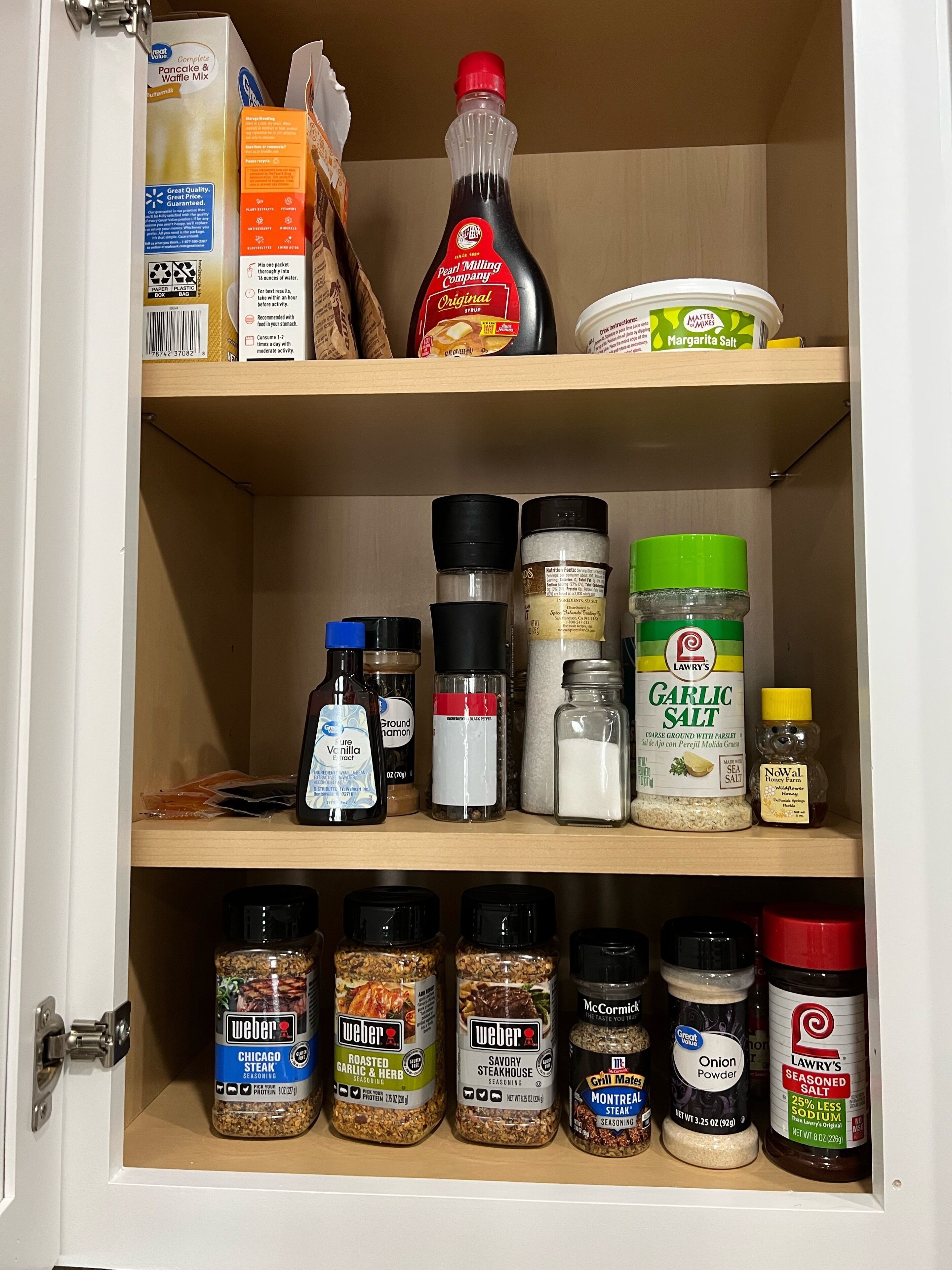 A pantry with various food items and condiments, including pancake mix, syrup, and several types of seasoning.