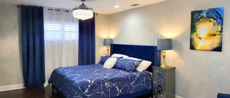 A bedroom with a bed, curtains, a chandelier, a nightstand, and a wall painting.