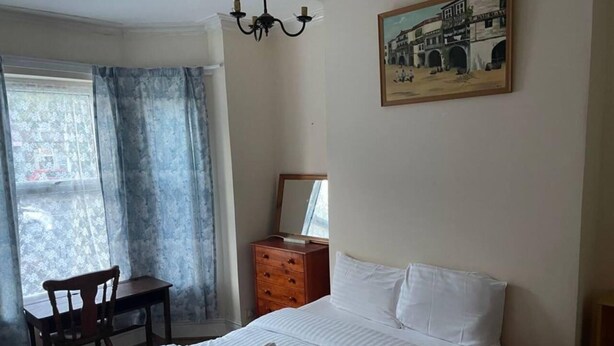 Een hotelkamer met een bed, een bureau, een stoel, een dressoir en een schilderij aan de muur.