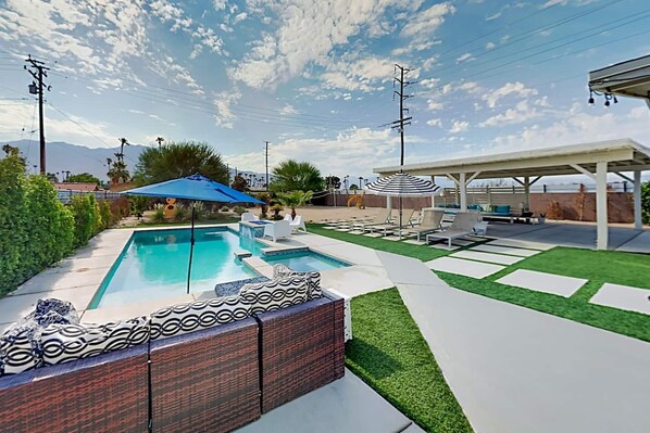 Un jardin avec une piscine rectangulaire, un patio couvert et une pelouse bien entretenue.