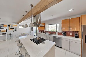 Une cuisine moderne dotée d’un îlot central, de luminaires suspendus et offrant une vue sur l’extérieur.