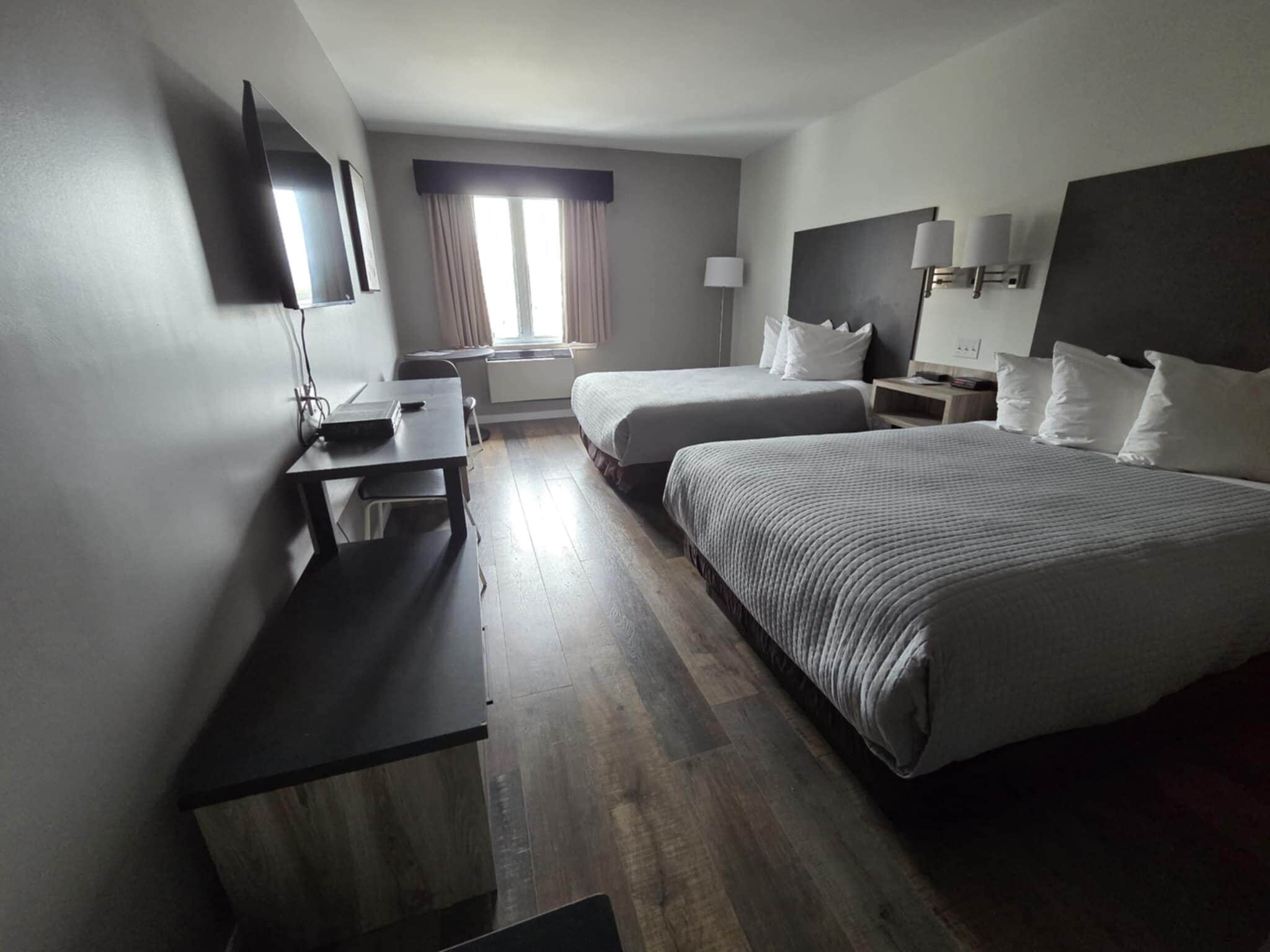 A hotel room with two beds, a desk, a chair, a TV, and a window with curtains.
