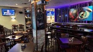 L’intérieur d’un restaurant est aménagé avec des tables et des chaises en bois, un tableau noir servant de menu et un grand écran de télévision diffusant un journal télévisé.
