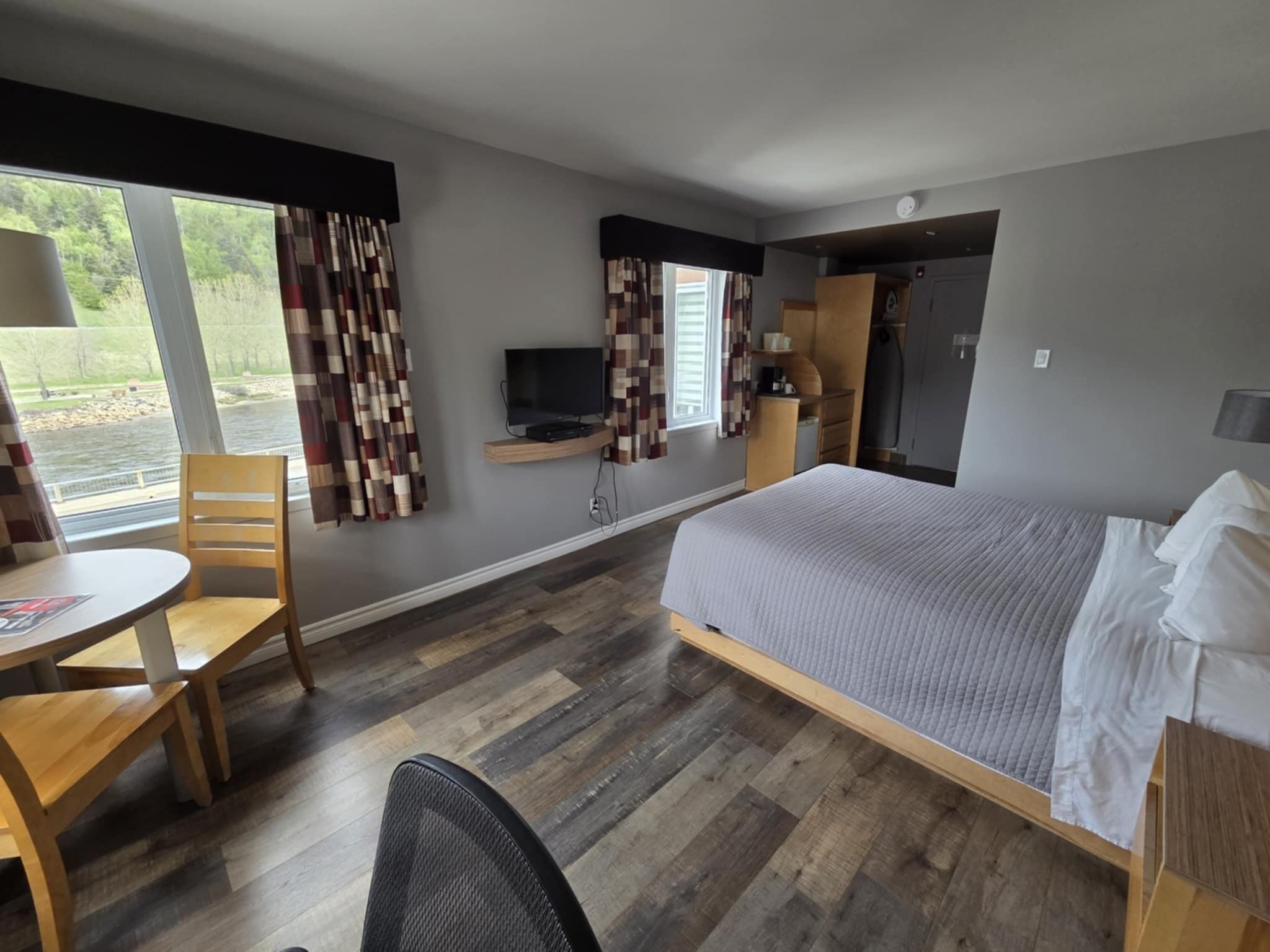Ein Hotelzimmer mit Bett, Schreibtisch, Stuhl, Fernseher und einem fensterbepflanzten Fenster.