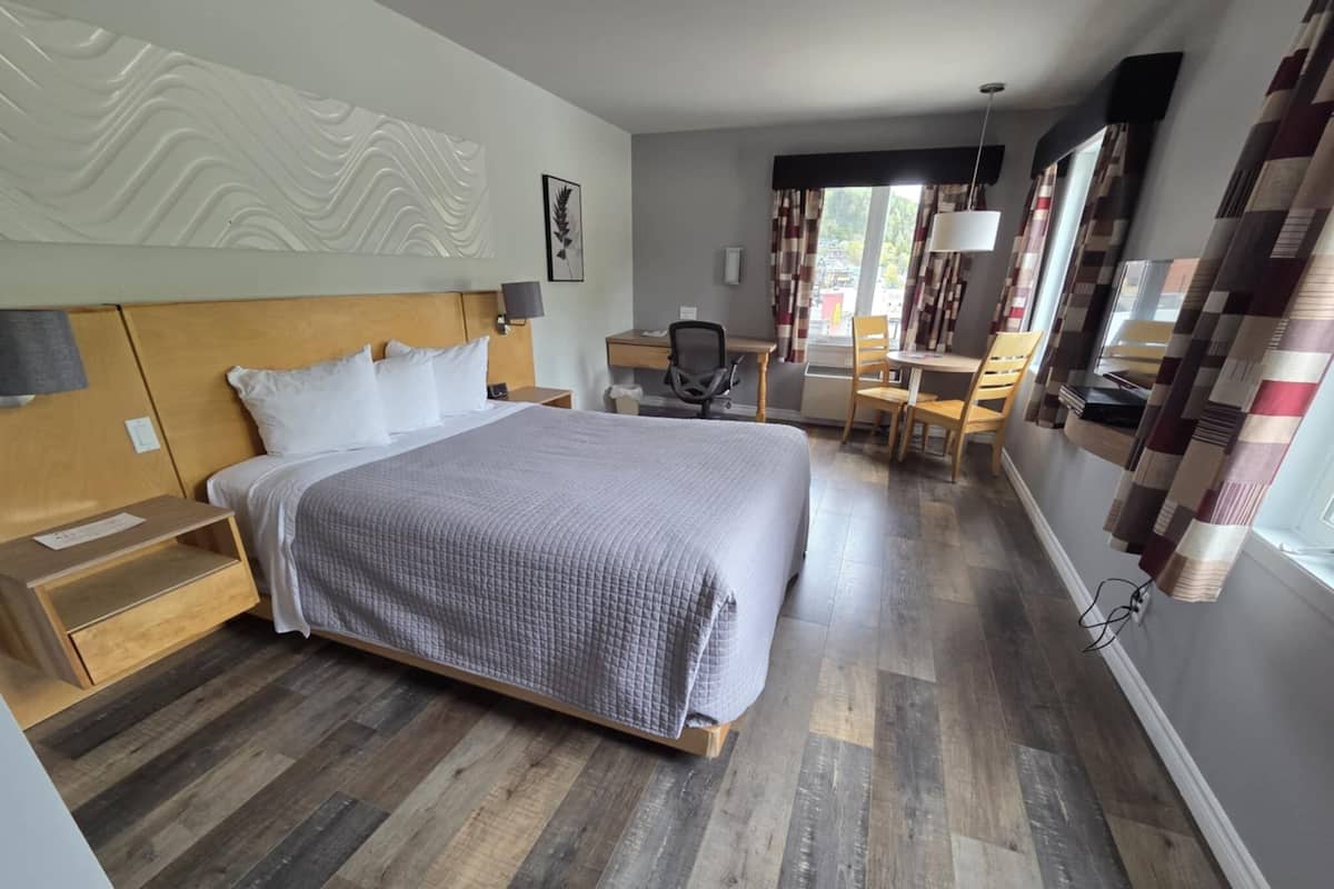 Una habitación de hotel moderna con una cama grande, cabecera de madera, un escritorio con silla y vistas al exterior a través de la ventana.