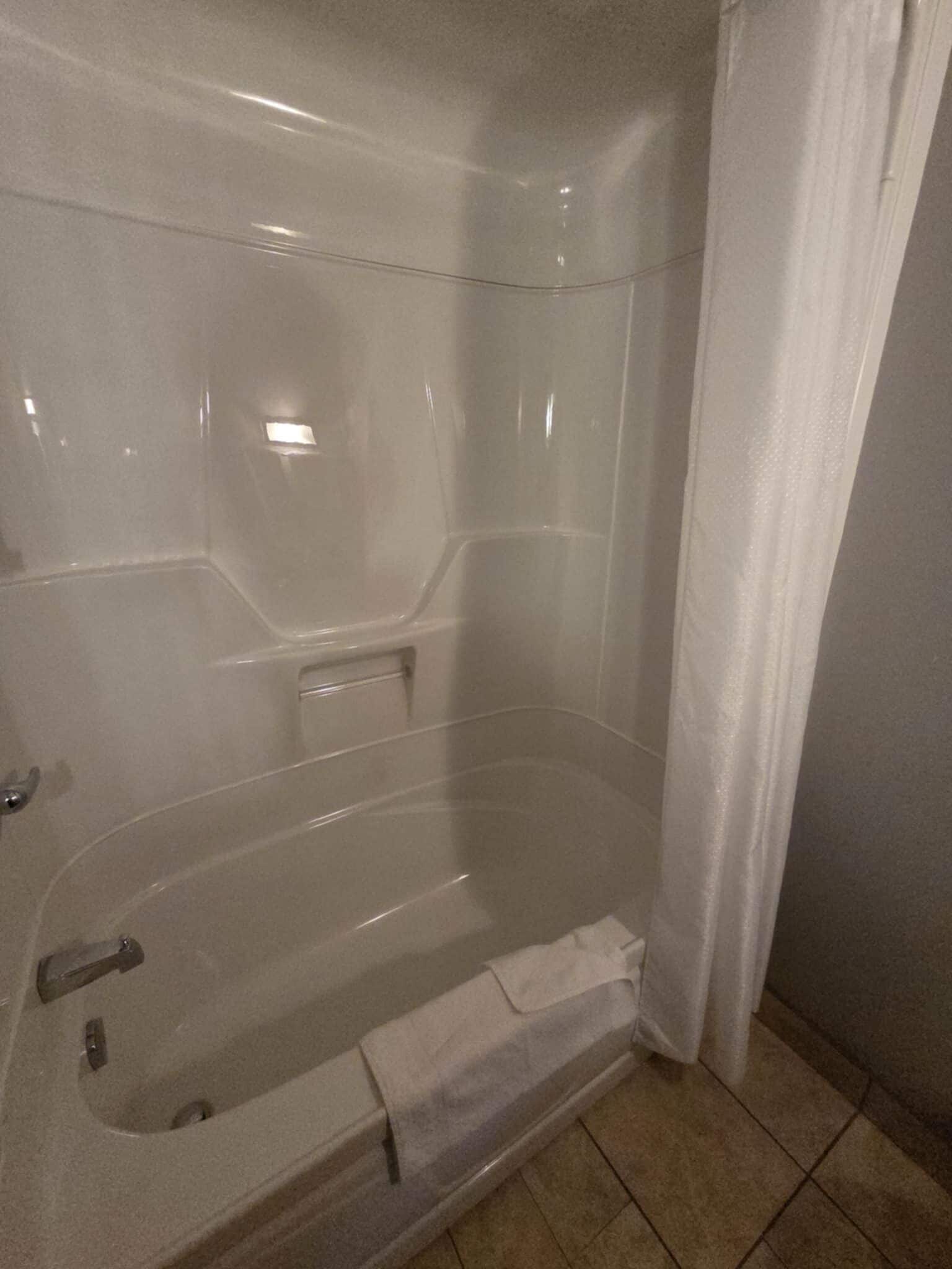 A clear glass-enclosed bathtub with a shower curtain, a towel, and a tiled floor.