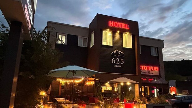 Un hôtel avec une enseigne indiquant le numéro de chambre 625, un pub et des tables à l’extérieur, décorées de guirlandes lumineuses.
