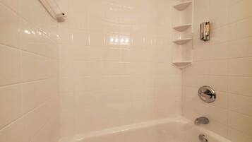 Un baño con paredes de azulejos blancos, una bañera y un cabezal de ducha.