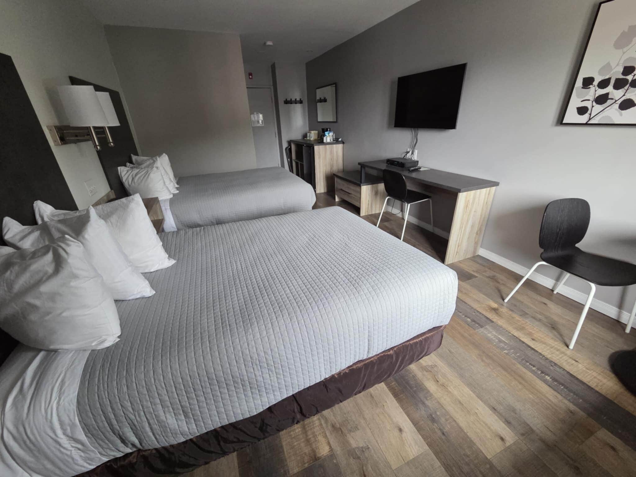 A hotel room with two beds, a desk, a chair, a TV, and a wall-mounted artwork.