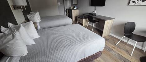Habitación de hotel con dos camas, un escritorio, una silla, un televisor y una obra de arte colgada en la pared.