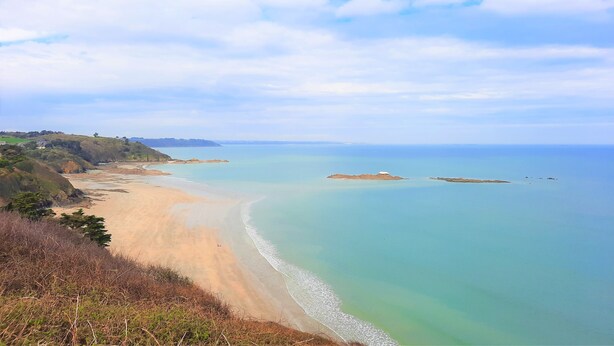 A coastal landscape with a sandy beach, calm sea, and distant hills.