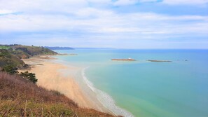 Un paysage côtier avec une plage de sable, une mer calme et des collines à l’horizon.