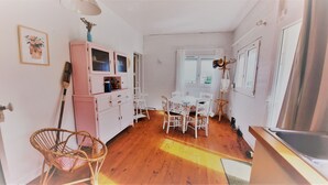 A small, cozy kitchen with white cabinets, a dining table, and a wicker chair.