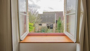 A window with a wooden sill and a view of a stone building with a tiled roof. - Parenthèse - Villenauxe LA Grande (VILLENAUXE LA GRANDE)