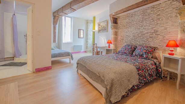 A bedroom with a large bed, a wooden ceiling, a brick wall, and a small desk with a lamp. - Parenthèse - Villenauxe LA Grande (VILLENAUXE LA GRANDE)