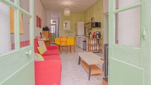 A cozy living room with a red sofa, a wooden dining table, and a kitchen area with a coffee machine and shelves. - Parenthèse - Villenauxe LA Grande (VILLENAUXE LA GRANDE)