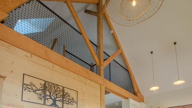 A spacious living area with a high ceiling, wooden beams, a blue sofa, a wooden coffee table, and a yellow armchair. - Le Chevrais - PAISY COSDON (PAISY COSDON)