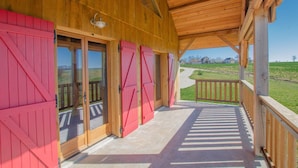A covered porch with red barn doors and a view of a green landscape. - Le Chevrais - PAISY COSDON (PAISY COSDON)