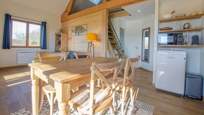 A spacious kitchen with a wooden table and chairs, a white refrigerator, and a staircase leading to an upper level. - Le Chevrais - PAISY COSDON (PAISY COSDON)