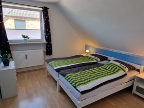 A bedroom with a bed, bedside table, lamp, window with curtains, radiator, and a potted plant.