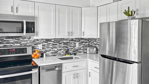 Una cocina moderna con electrodomésticos de acero inoxidable, armarios blancos y salpicadero de azulejos.