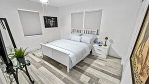 Un dormitorio con cama, mesitas de noche, ventilador de techo y una planta en maceta.
