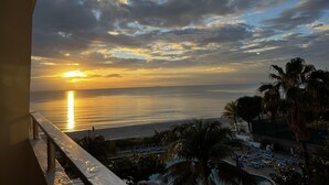 A sunset view from a balcony overlooking a beach with lounge chairs and palm trees. - Beautiful Oceanview Modern Hotel Room W/ Balcony (Fort Lauderdale)